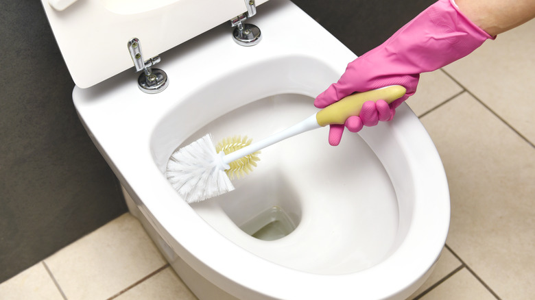 Hand with pink glove cleaning toilet with scrubber