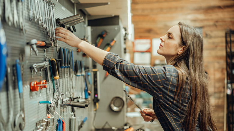 A woman looking at tools that are hanging on the wall.