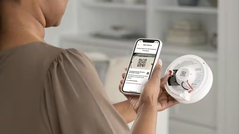 Person scanning QR code on back of smart smoke alarm with phone