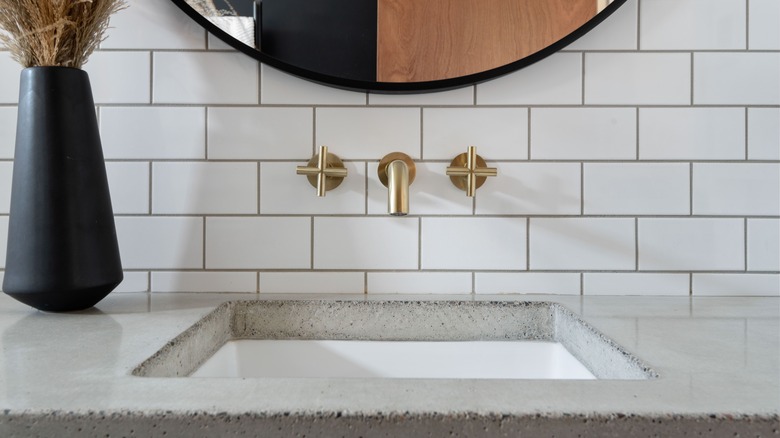 A brass wall faucet is installed over white subway tile with dark grout