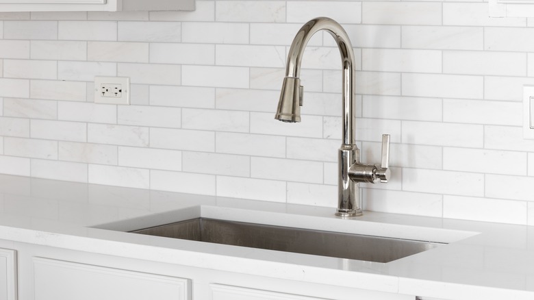 A chrome kitchen faucet is surrounded by white tile