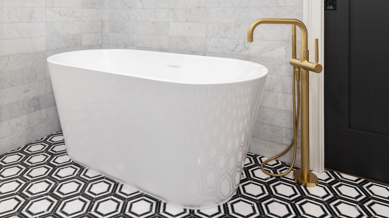 A white freestanding tub sits on a bold black and white patterned floor