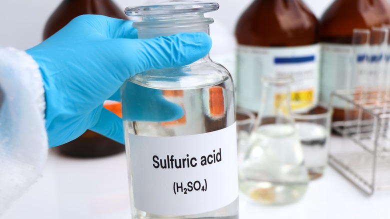 A hand holding a bottle of sulfuric acid