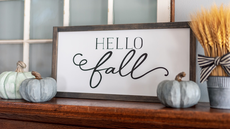 A sign reading "Hello Fall" is surrounded by minature pumpkins and a dried wheat arrangement