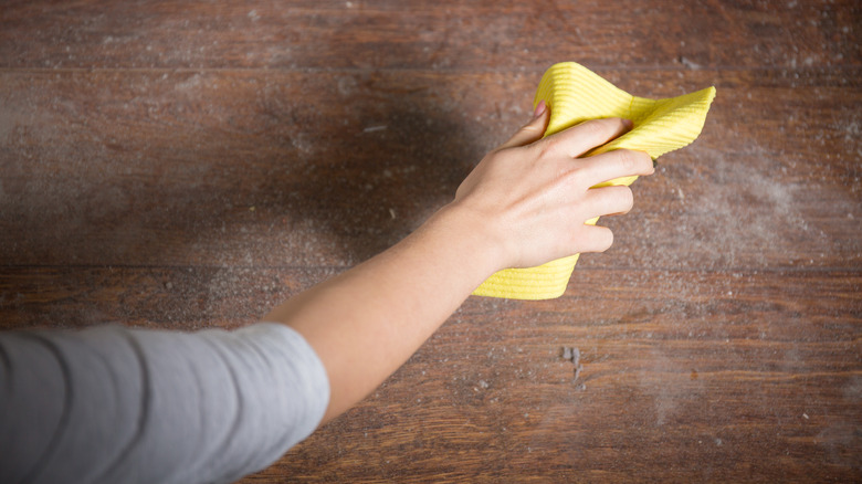 woman dusting dusty wood surface with yellow microfiber