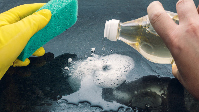 person pouring vinegar on surface while holding sponge