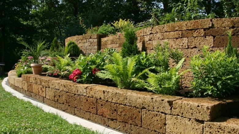 A two-tier retaining wall made of large stones with garden beds growing a variety of plants