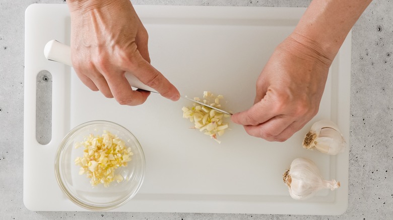 garlic being chopped on a plastic cutting board