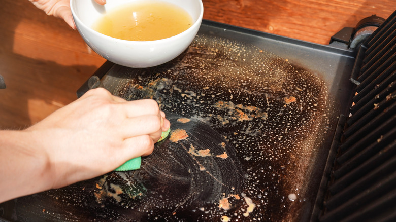 Cleaning small grill with bowl of soapy water and rag