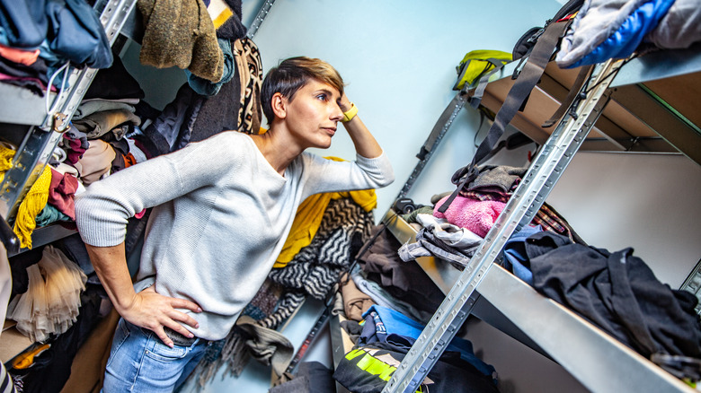 Frustrated person looks through messy clothes closet