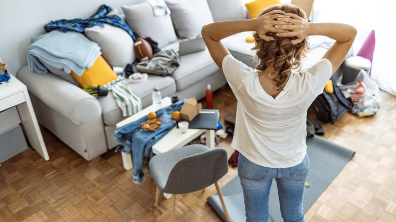 A woman with hands on her head looking at a cluttered room