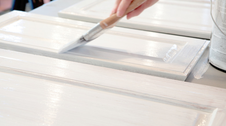 A person applying a second coat of white paint to cabinet doors