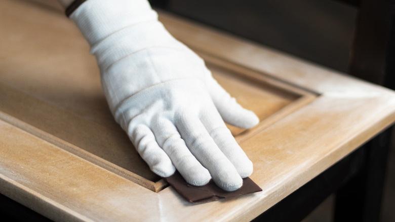 Gloved hands sanding a cabinet door with sandpaper