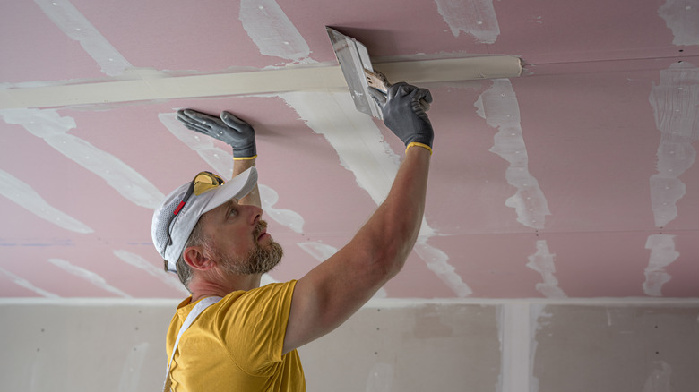 Professional worker applying drywall on ceiling