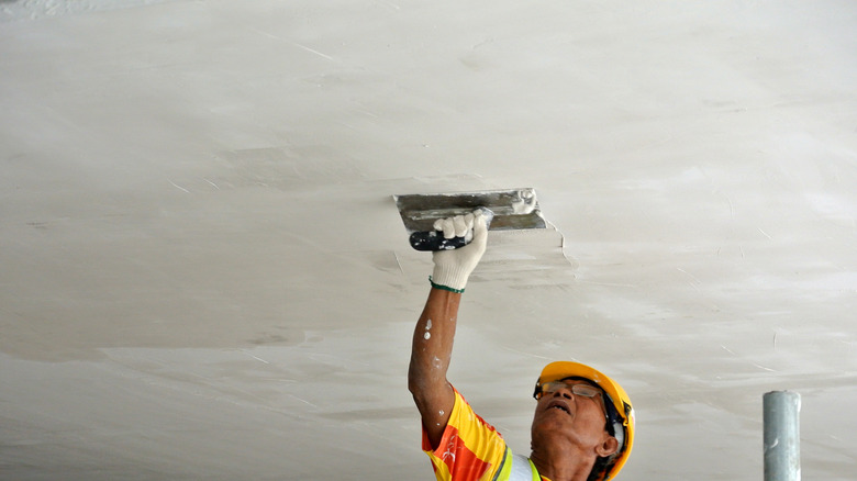 Worker applying skim coat over ceiling