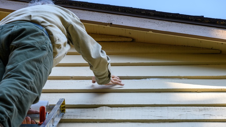 A person on a ladder checking out the siding