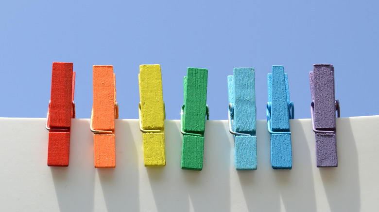 Seven colorful wooden clothespins are clipped to a white board in a line