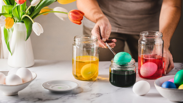 A person spoons a dyed blue Easter egg out of a jar of dye with two other jars with eggs in them on either side