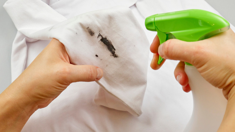 woman spot cleaning white linen shirt with spray cleaner