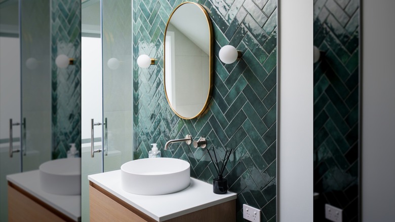 Glossy teal tiles above white round sink with gold mirror