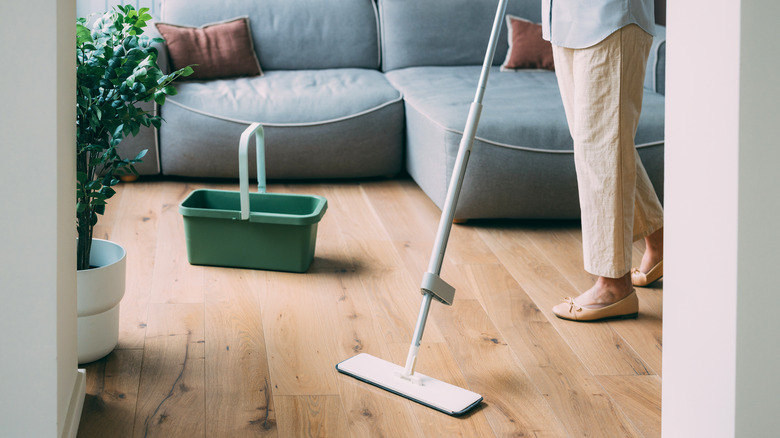 Person mopping wooden floor with white mop and green bucket