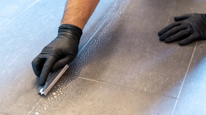 Gloved hands cleaning grout