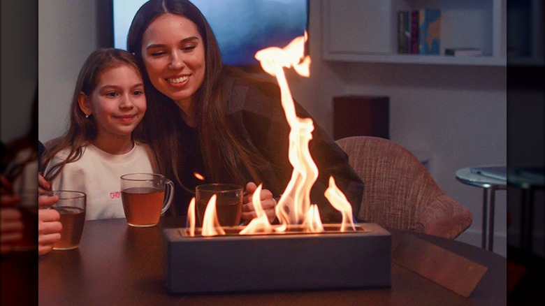 A mother and daughter sitting by a tabletop fireplace