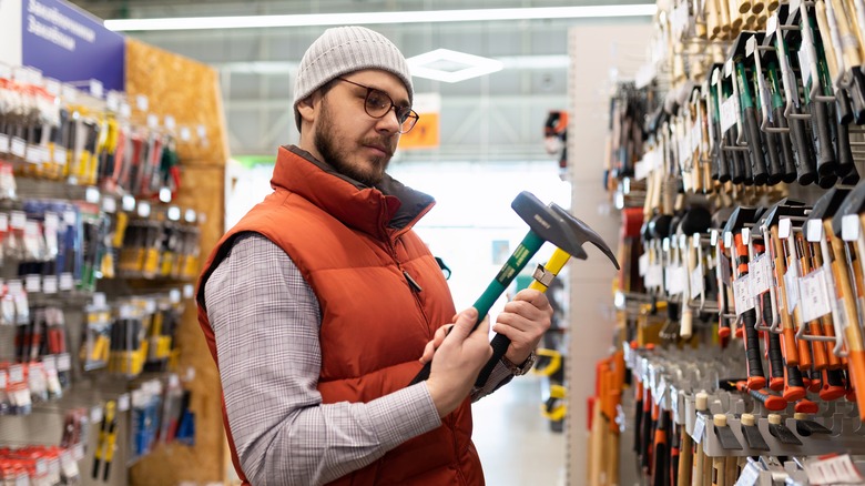 Man considers two hammers at hardware store