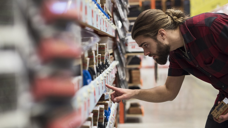 A man looks closely at the price of a tool in a hardware store aisle