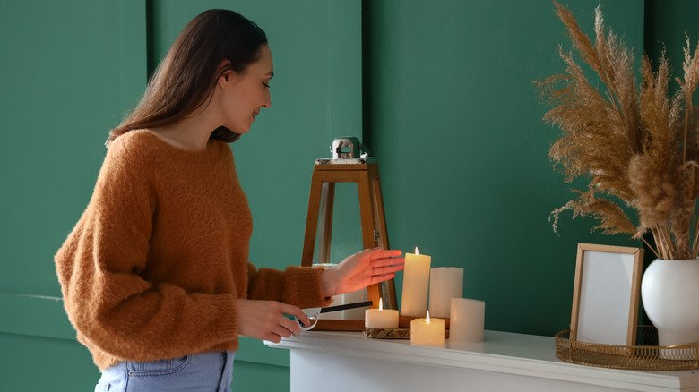 Woman in a brown sweater lighting candles on a freshly-styled white mantelpiece