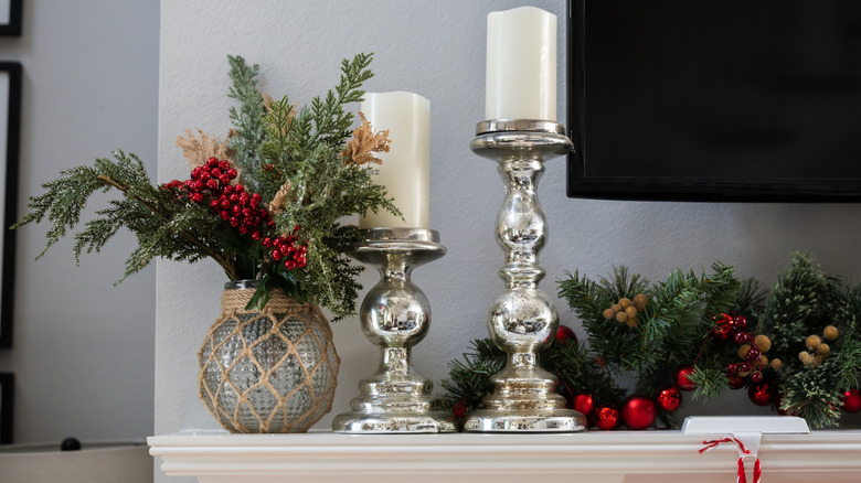 A white mantel with a TV above decorated for the winter with candles, evergreen foliage, and silver candlesticks