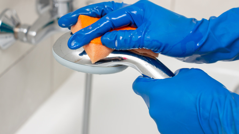 blue gloves cleaning a showerhead