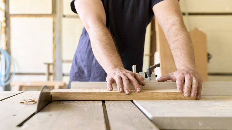 Man in a black t-shirt cutting a hardwood board on a table saw