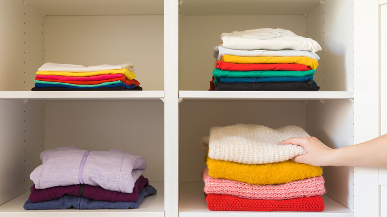 Hand reaching for folded sweater on cube shelving unit full of clothing