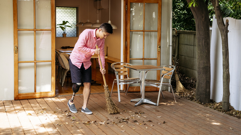 man sweeps leaves from patio