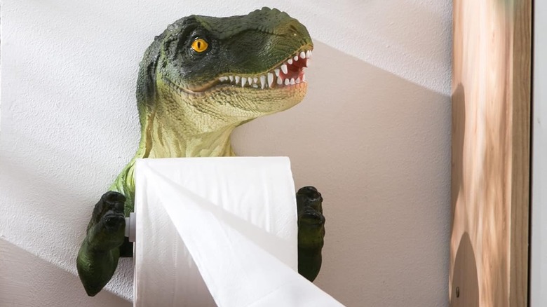 A dinosaur toilet paper holder that has the T-Rex holding the toilet paper in its hands