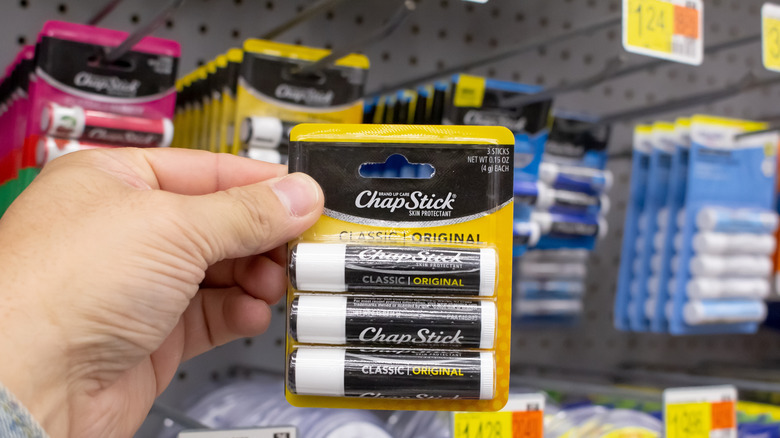 A person holds up a packet of new Chapstick tubes in a store.