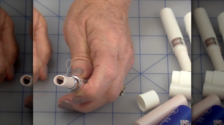 Woman inserting sewing supplies into an old Chapstick container.