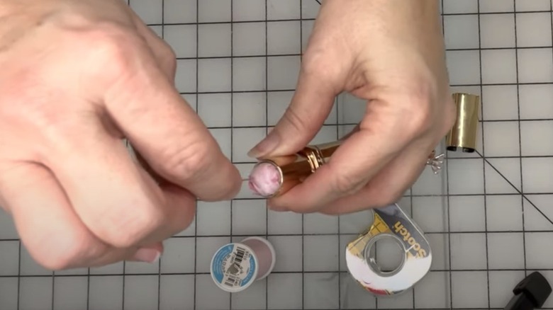 Woman inserting soft material into an old lip balm tube to make a mini pin cushion.