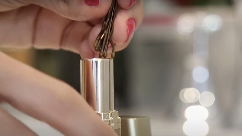 Woman filling an empty lip balm tube with bobby pins.