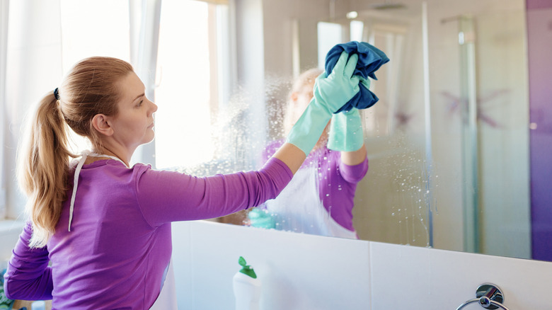 Woman cleaning bathroom mirror