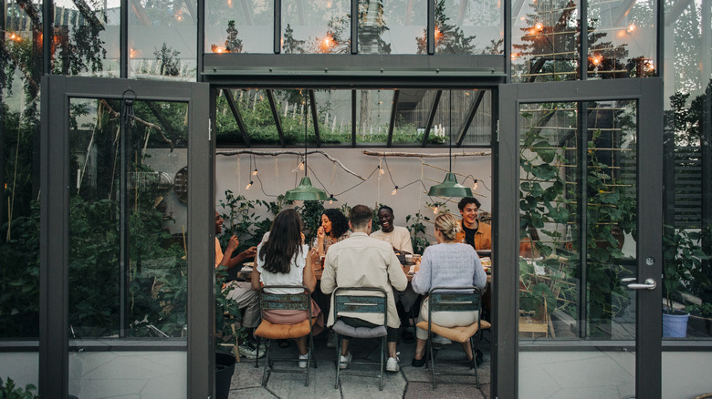 People dining in a backyard greenhouse repurposed as a dining area