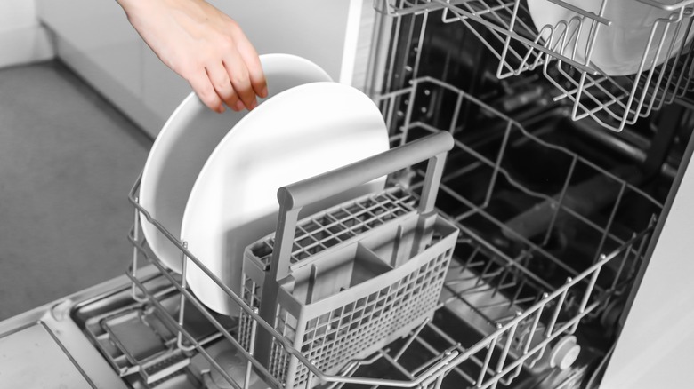 Woman's hand reaching a white plate in dishwasher