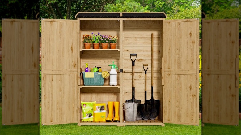 Both doors of a wooden storage shed are open to display the gardening tools inside