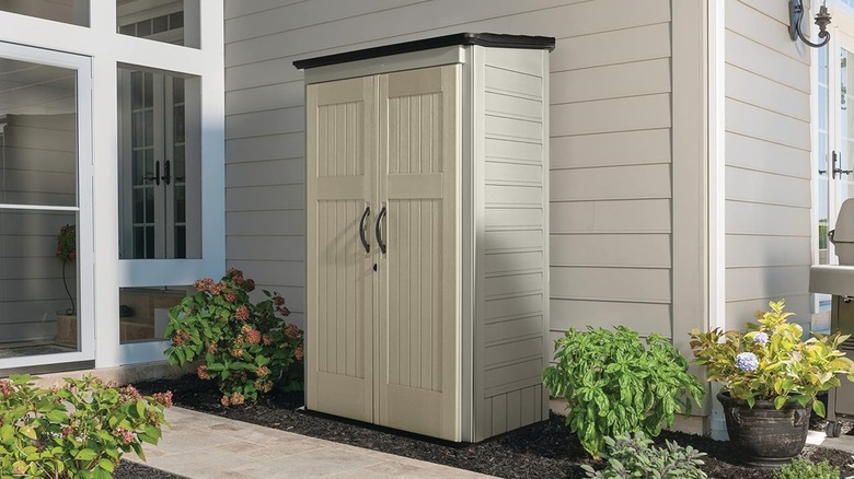 A tall cream-colored Rubbermaid shed is surrounded by plants