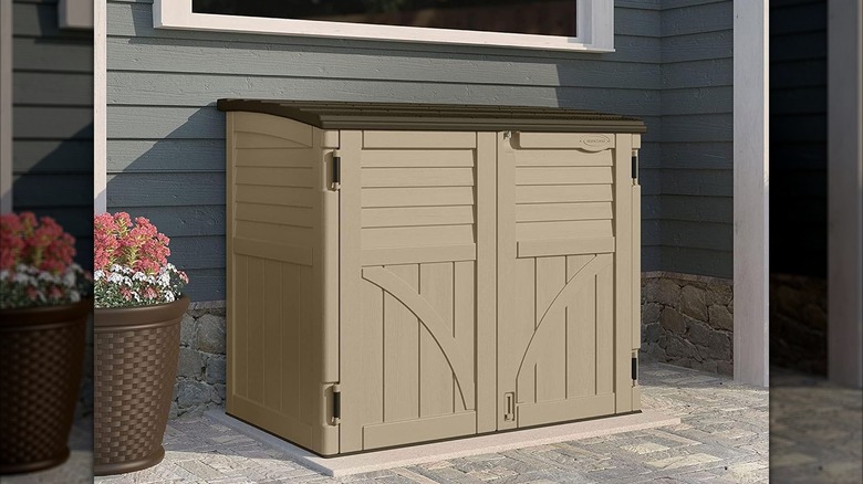 A small brown garden shed sits on a patio