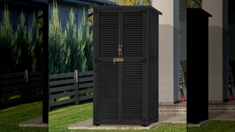 A black lockable shed with plantation shutter-style doors sits on a concrete patio