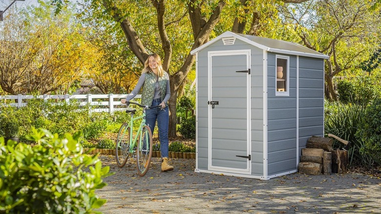 A woman walks a bicycle next to a garden shed