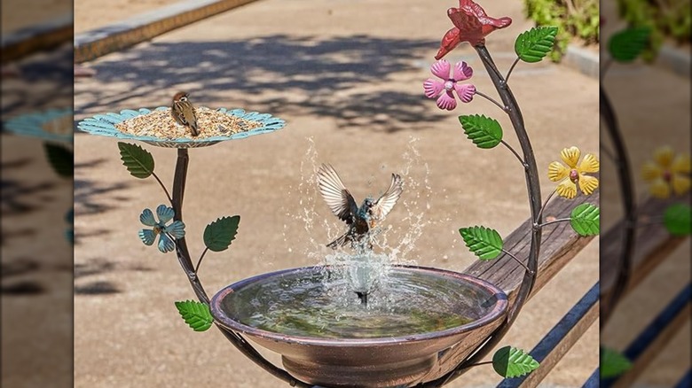 An elaborate solar bird bath with bird feeder and leaves and flowers as decoration