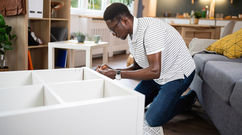 Man assembling a bookshelf on living room floor